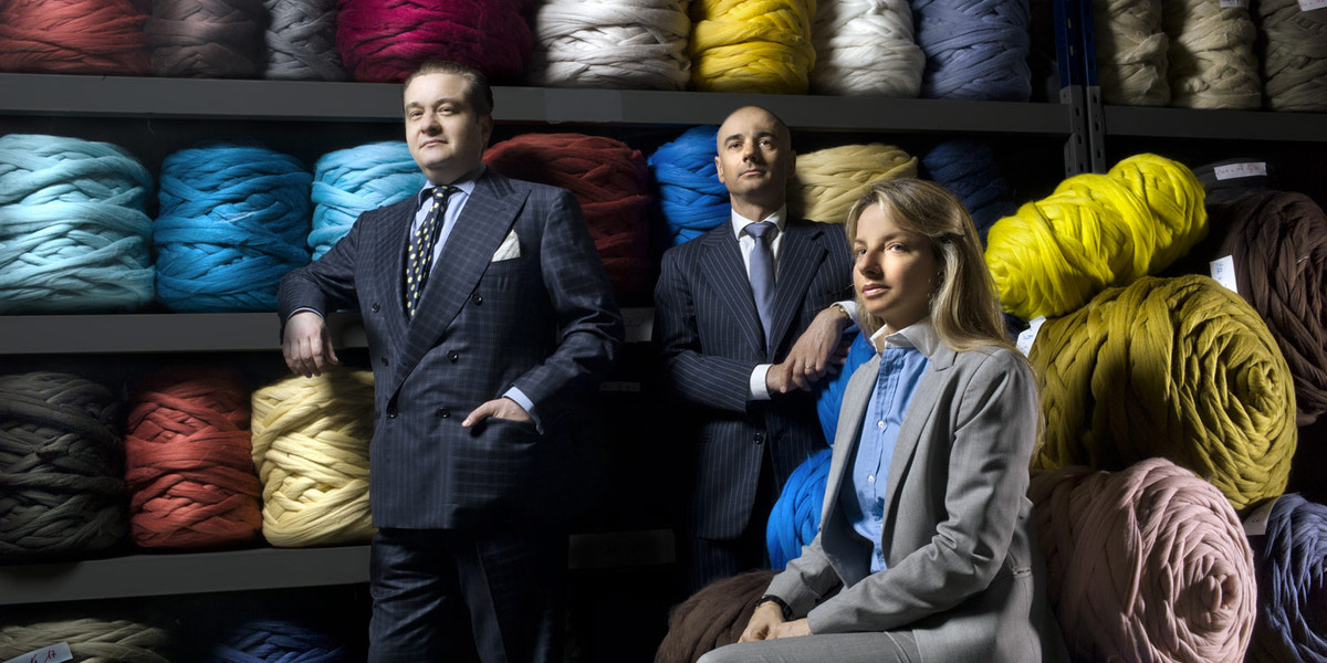Trei bărbați în ținute elegante, în fața unei selecții de fire colorate