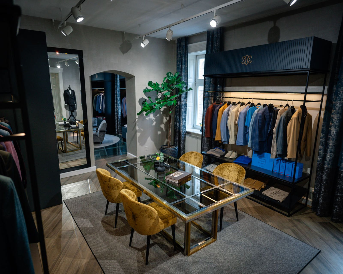 Masă de consultanță din sticlă și fotolii muștar, lângă o selecție de sacouri în showroomul Consiglieri