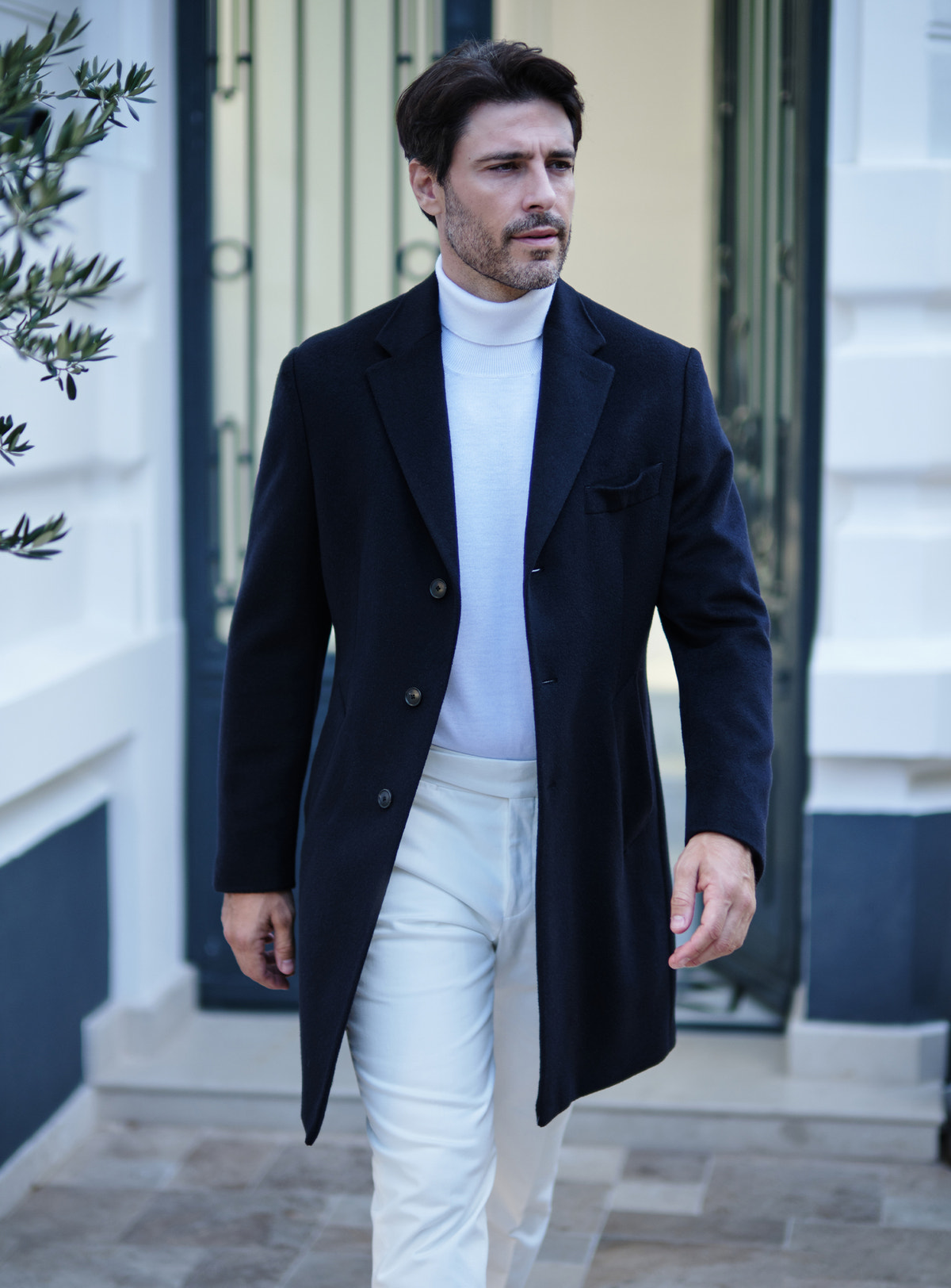 Palton bleumarin Consiglieri cu rever crestat, purtat cu maletă și pantaloni albi