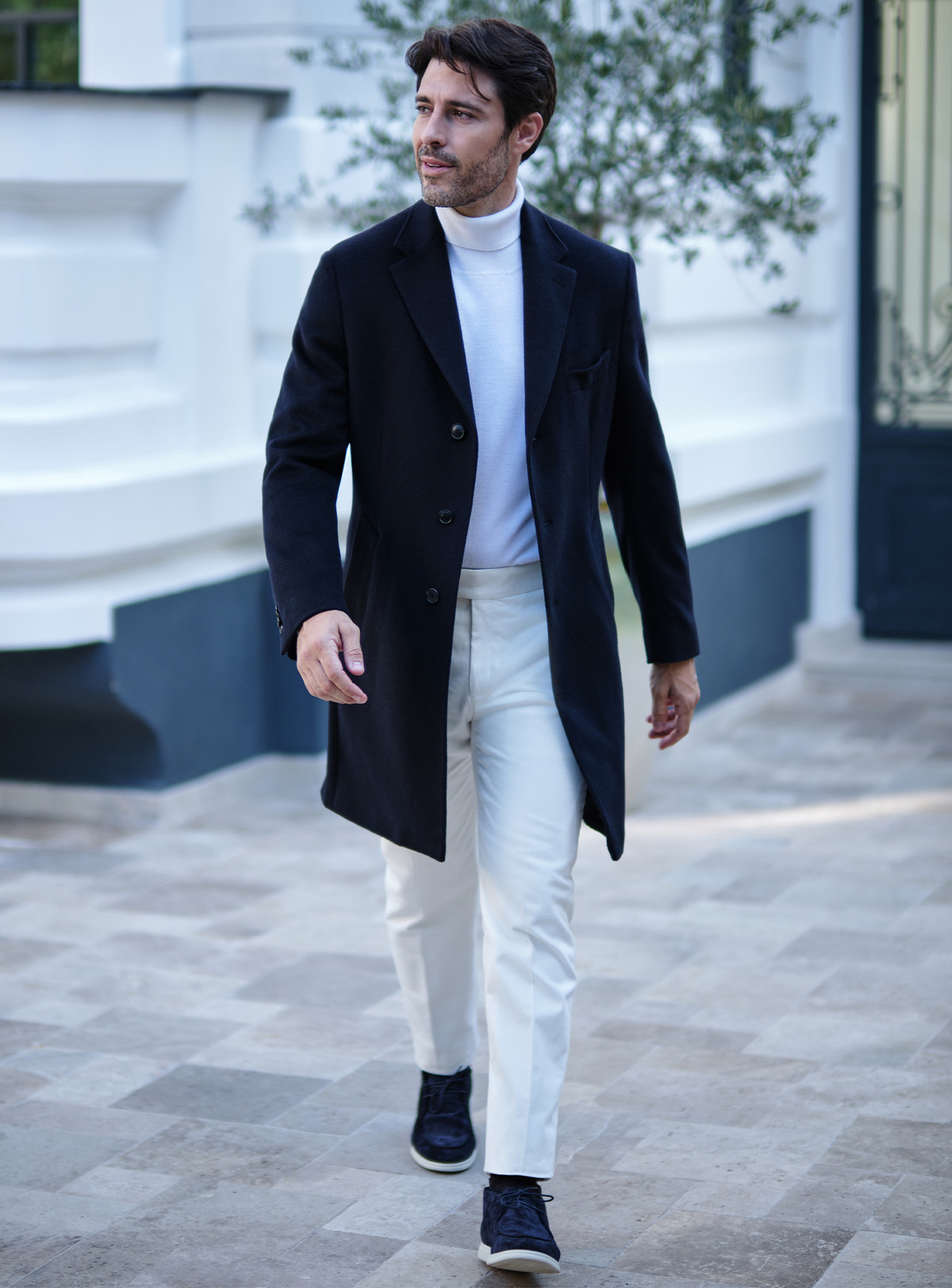 Palton bleumarin Consiglieri cu rever crestat, purtat cu maletă și pantaloni albi