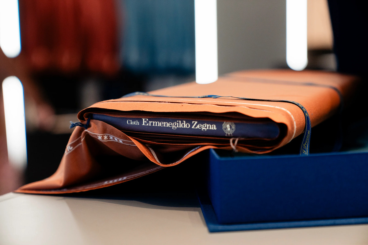 Țesătură cu eticheta Ermenegildo Zegna, așezată peste albumele de prezentare.