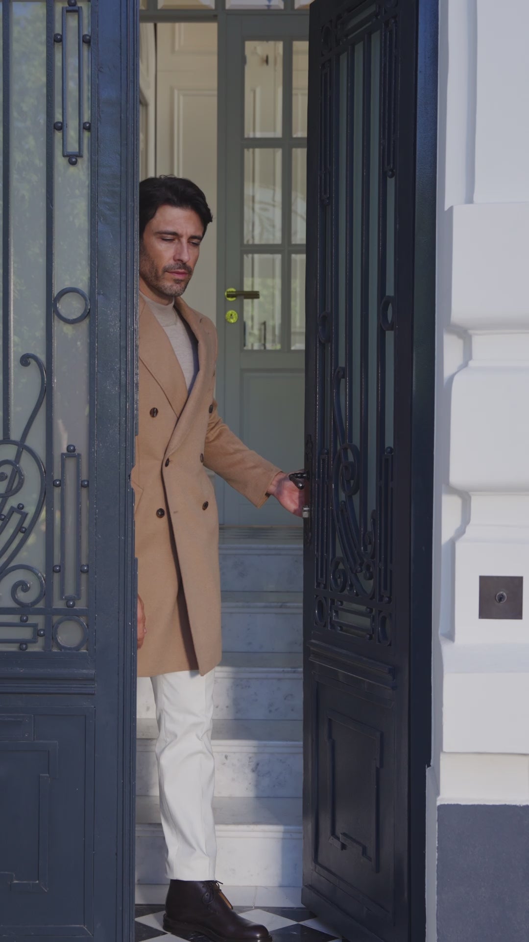 Palton camel cu pantaloni deschiși la culoare, în dreptul unei intrări ornamentate