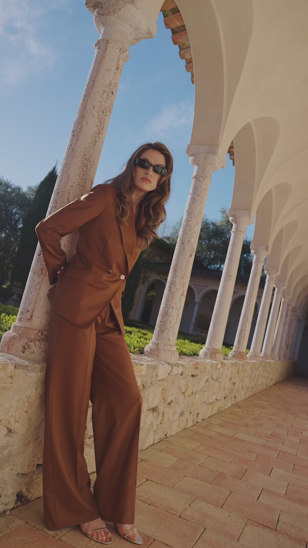 Costum feminin Ambre Consiglieri, în tonuri de arămiu, lângă coloane deschise
