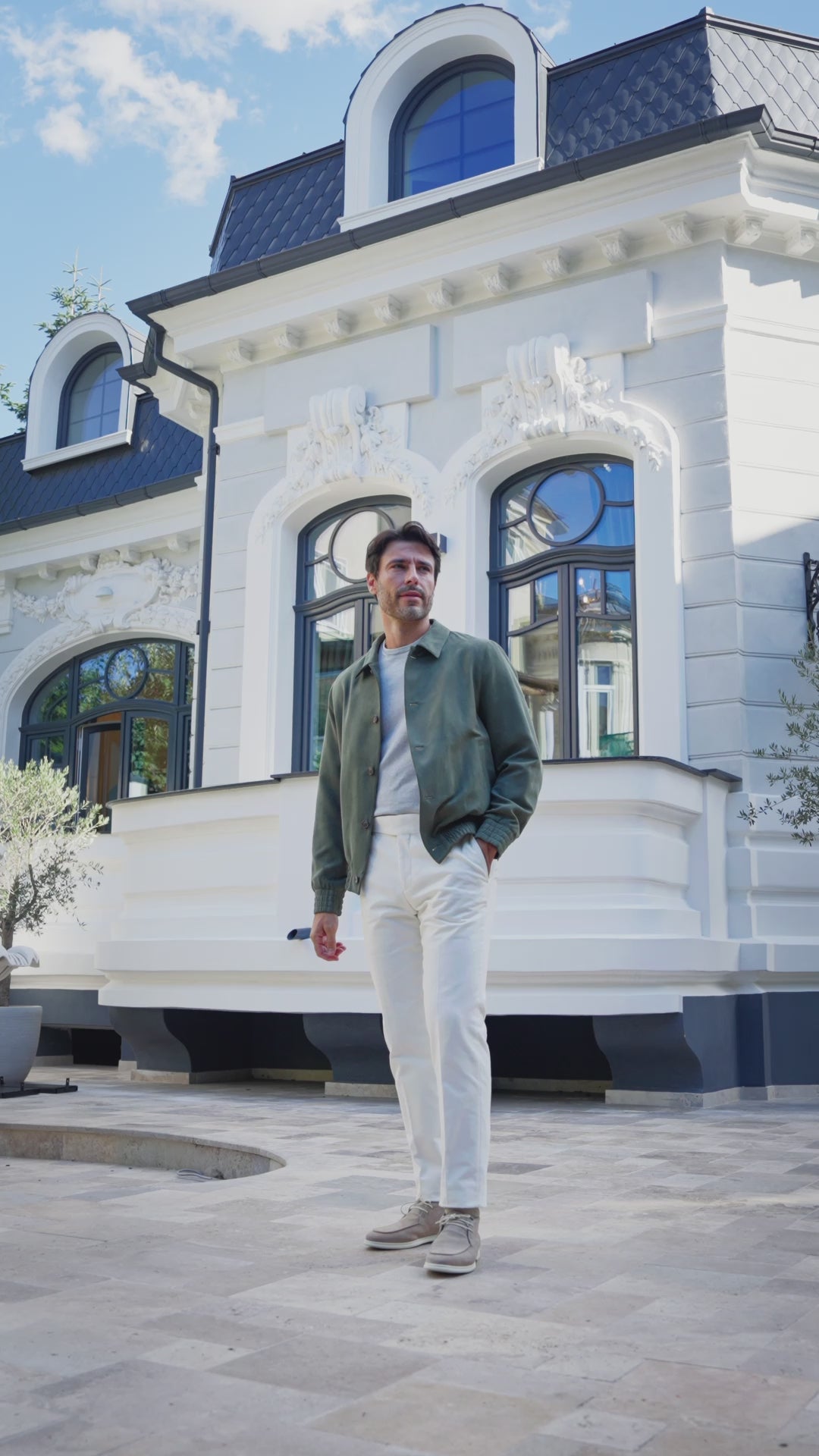 Jachetă verde cu pantaloni albi, purtată în fața unei clădiri cu ferestre arcuite
