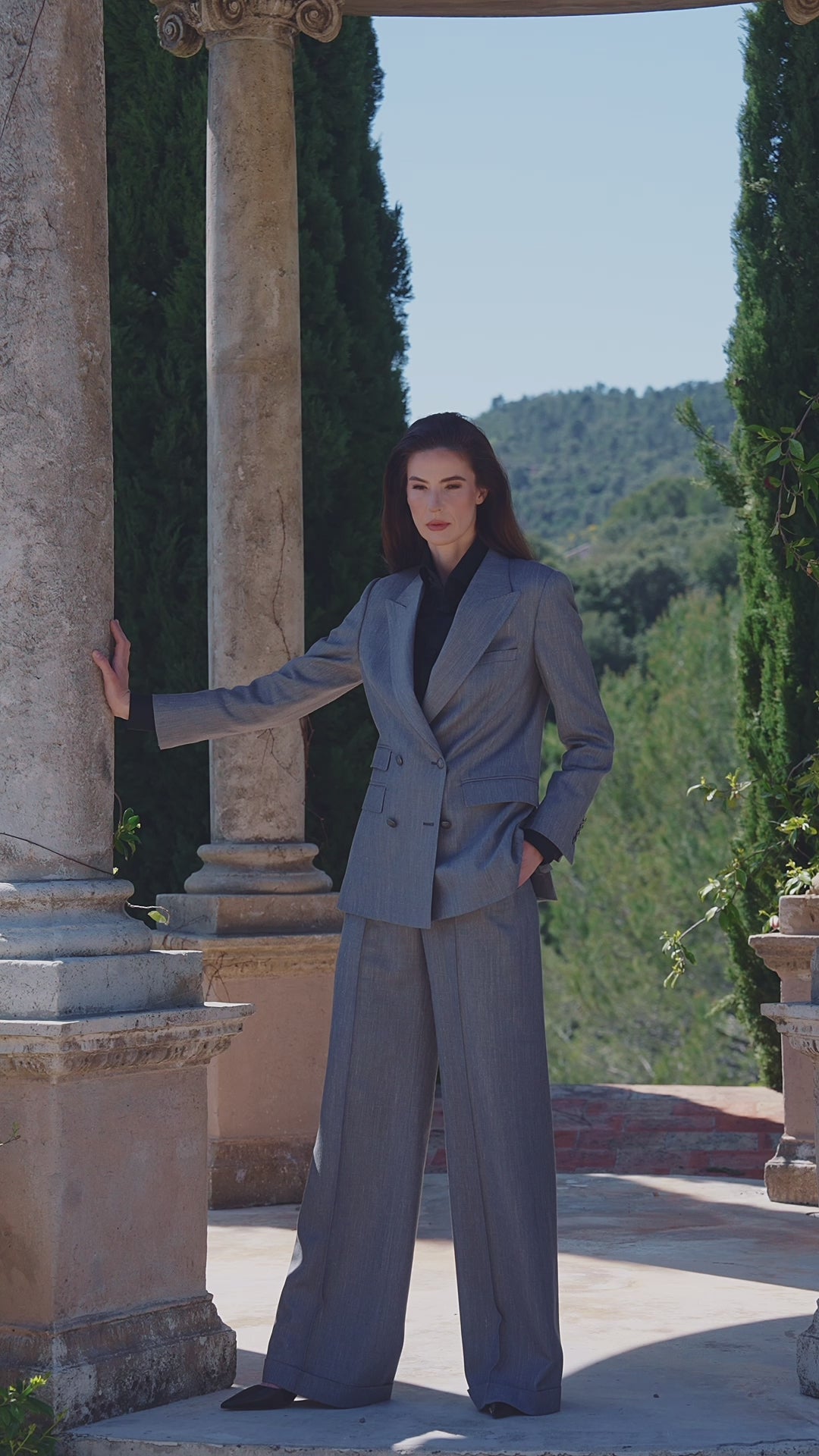 Costum feminin gri la două rânduri de nasturi, lângă o coloană de piatră