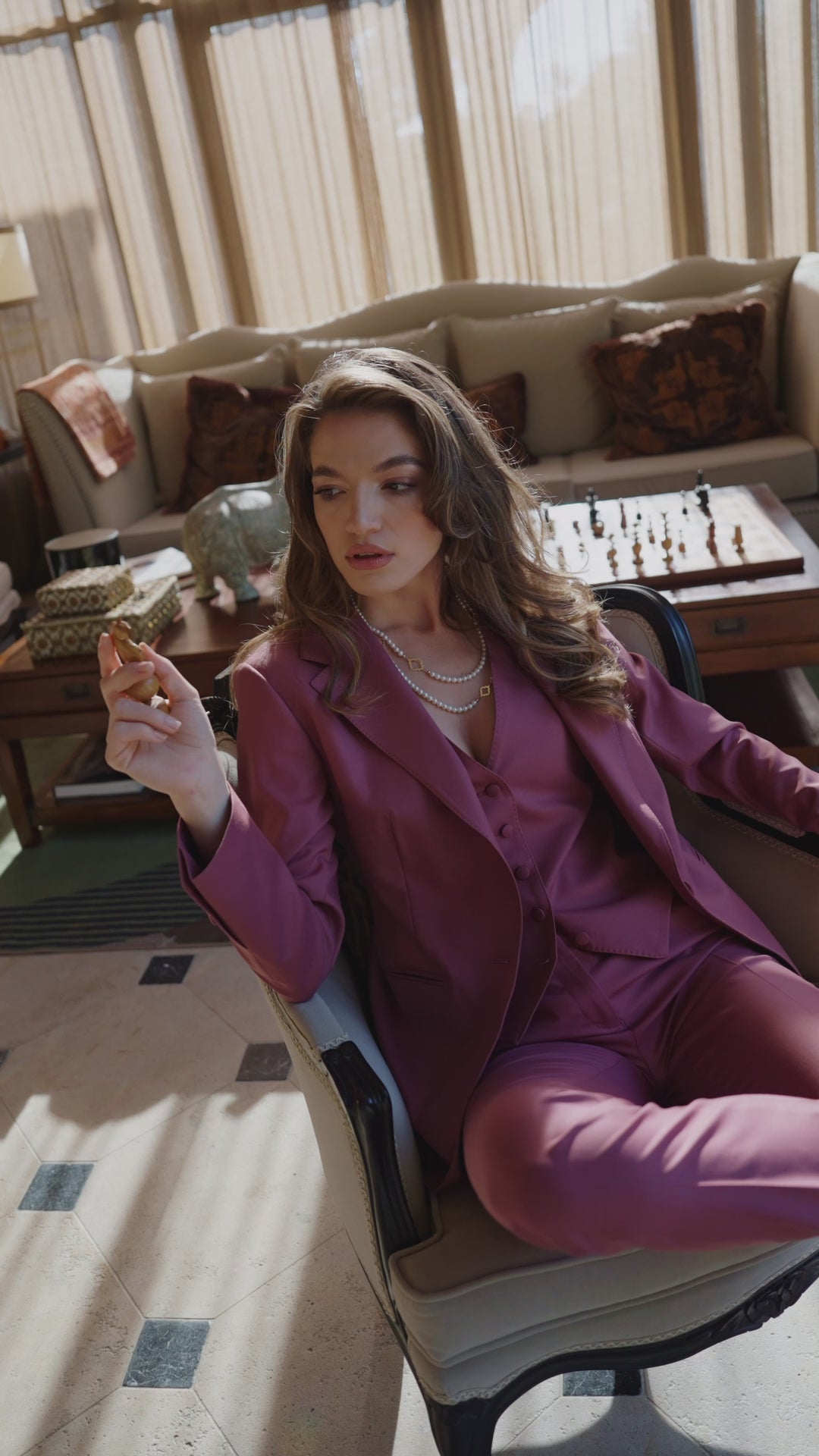 Femeie în costum violet, așezată într-un salon și ținând un pahar