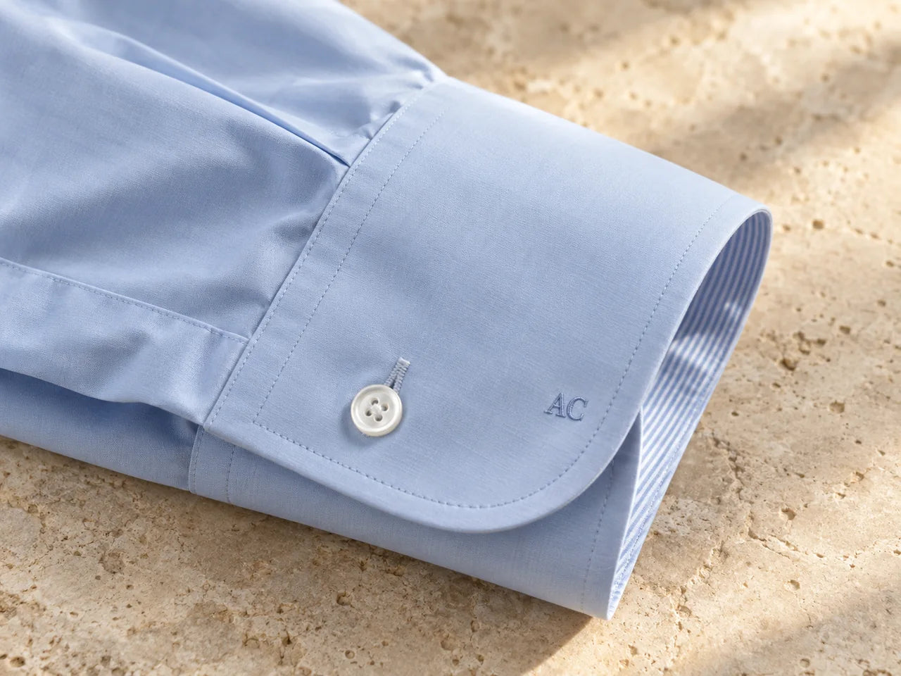 Monogramă discretă brodată pe o manșetă de cămașă bleu